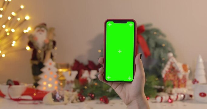 Woman hand showing mobile phone iPhone 11 Pro Max with green screen. Christmas spirit, holidays, congratulations and celebrations concept. POV. 4k footage