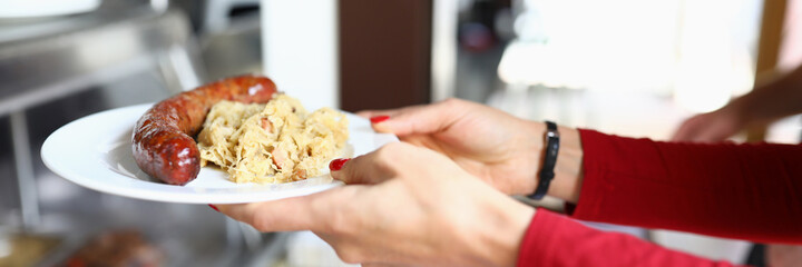 Female hands hold plate with lunch on it sausage and stewed cabbage in bistro. Lunch menu of cafes and restaurants concept