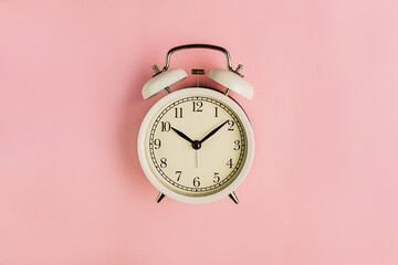 Old school white alarm clock on the pink background. Flat lay, top view.
