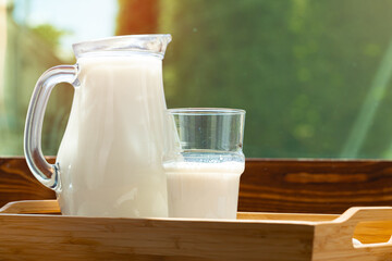 Pitcher of milk on wooden table against blurred foliage background