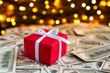 Red gift box on USA 100 dollar bills on the blurred lights background. American dollar. Christmas and New Year money present. Gift cost. Hundred. Finance and business concept. Christmas shopping
