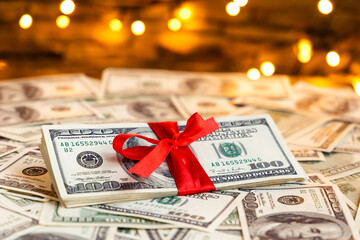 USA 100 dollar bills with red ribbon on the blurred lights background. American dollar. Christmas and New Year money present. Gift cost. Hundred. Finance and business concept. Christmas shopping