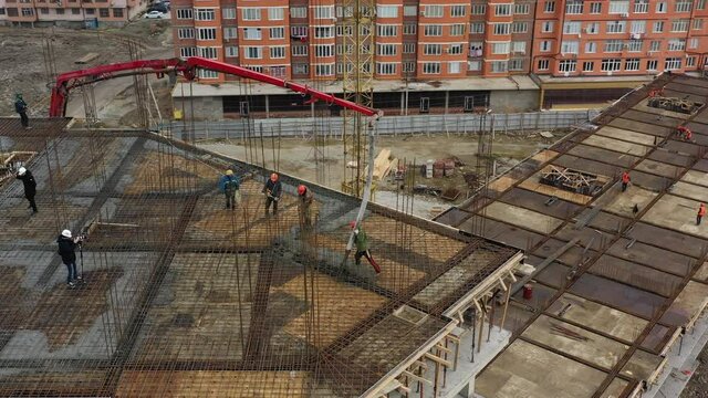 Skillful construction workers put layer of liquid concrete on upper platform pointing boom of self-propelled pump aerial view