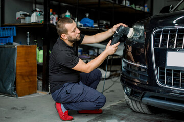 Fototapeta na wymiar Car detailing series, polishing concept. Professional male auto service worker, waxing and polishing headlight of black car with orbital polish machine
