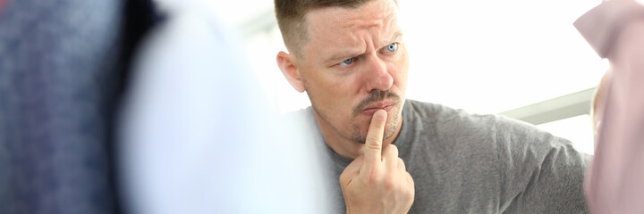 Pensive man looks at hanger with clothes. Men's wardrobe and stylish clothing concept