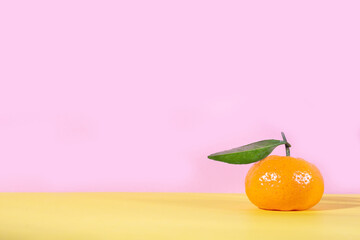 Ripe orange tangerine with leaf on pink and yellow background copy space