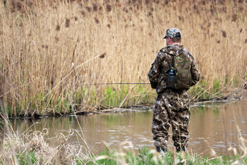 Fisherman in hunting clothes standing with a fishing rod, selective focus. Man angling on the river...