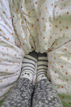 Feet in cute fuzzy socks on a bed. Top view, selective focus.