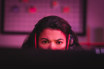 Focused african american gamer in headset looking at computer on blurred foreground