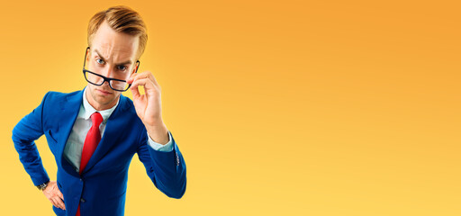 Funny skeptic businessman in blue confident suit and red tie, looking through glasses, copy space empty area for some text or slogan, advertising or slogan, over yellow-orange color background. - obrazy, fototapety, plakaty