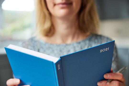 Close Up Of Woman Opening New Year 2021 Diary On Table At Home