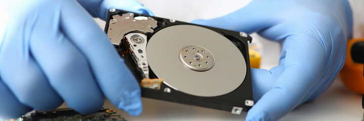 Gloved master holds hard drive away from computer. Computer repair service concept