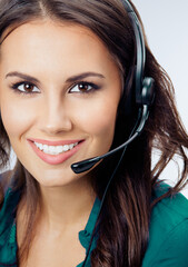 Happy smiling female phone operator in headset, green confident clothing, over grey background....