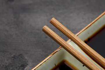 Bowl with soy sauce for sushi and chopsticks on black background