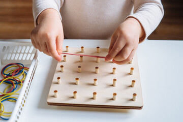 Child is playing with wooden geoboard at home. Children's creative game for early development and...