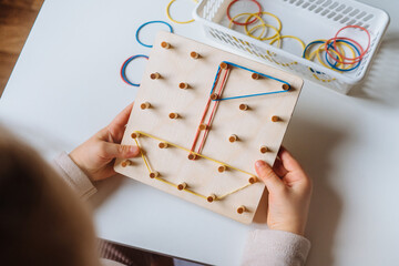 Child is playing with wooden geoboard at home. Children's creative game for early development and...