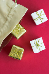 Little golden and white presents falling out of a golden bag on red background; christmas presents; decoration