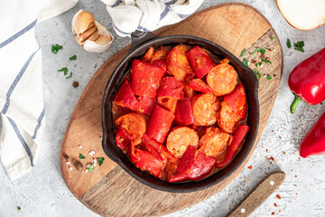 Sausages stewed with peppers, onions and tomatoes in a pan on a gray concrete background. Traditional Hungarian food lecho with sausages and vegetables.