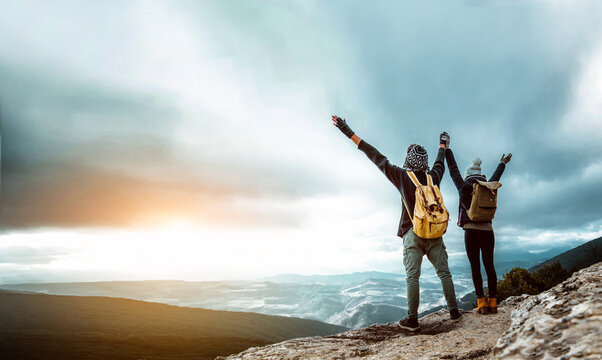 Hikers With Arms Up Celebrating Success On The Top Of A Mountain At Sunset - Couple Hiking Rock - Success, Teamwork And Sport Concept