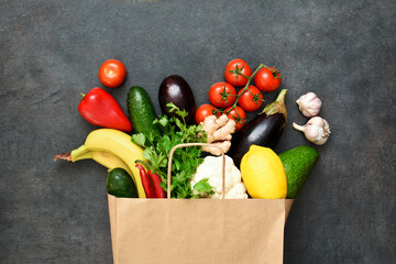 Fresh vegetables, fruit and greens in craft paper shopping bag on black rustic background. Eco shopping and food delivery concept.  A concept of proper nutrition delivery.