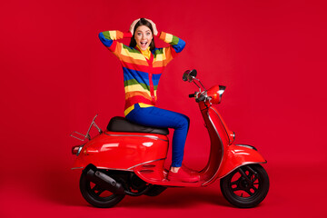Obraz na płótnie Canvas Portrait of pretty cheerful amazed girl sitting on moped having fun vacation isolated over bright red color background