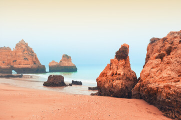 Fototapeta na wymiar MIsty morning on the shore of Atlantic ocean in Algarve, Portugal. Red sand with turquoise water. Famous travel destination