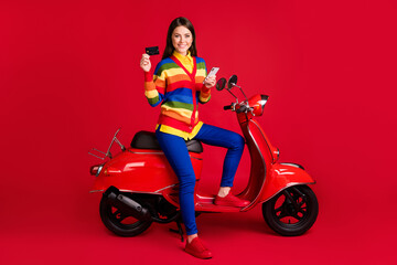 Fototapeta na wymiar Photo portrait of woman holding phone credit card in hands sitting on retro scooter isolated on vivid red colored background