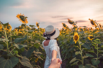 Beauty woman in white dress holding hands a couple in sunflower field at evening