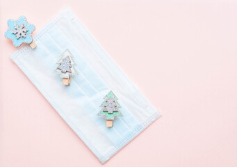 medical protective face mask and figures of Christmas trees and snowflakes wooden on a pink background. Decor Christmas and New Year 2021. Holidays self-isolation and coronavirus pandemic concept