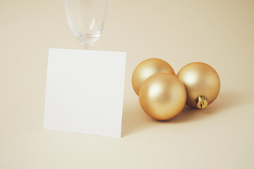 Creative New year composition with white paper card, Champagne glass and gold Christmas baubles. Minimal holiday concept. 