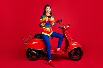 Obraz na płótnie Canvas Photo portrait of excited screaming woman holding credit card in two hands sitting on scooter isolated on vivid red colored background