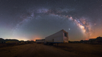 night panorama of the arch of the milky way over the trailer of an abandoned truck in the desert