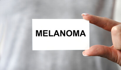The girl holds in front of her a business card with the text of MELANOMA.