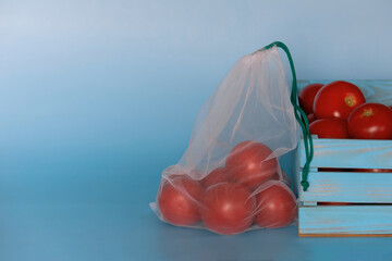 tThe reusable organza net bag for shopping, wooden box with tomato are on the blue background....