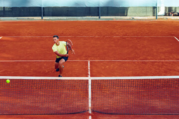 Young handsome man playing tennis on the tennis court