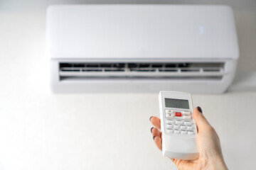 Fototapeta premium Room air conditioning. Air conditioner remote control in female hands. Copy space.
