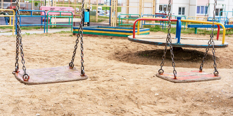 Fototapeta na wymiar wooden swings on rusty chains and carousel on playground
