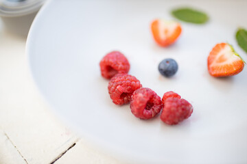 Smiling face made with berries and mint leaves on a plate