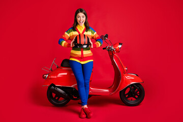 Fototapeta na wymiar Photo portrait of screaming girl holding helmet in two hnads sitting on scooter isolated on vivid red colored background