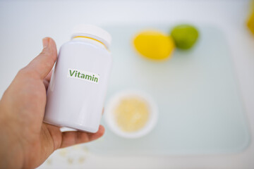 Hand holding a bottle of vitamins above a lemon and a lime