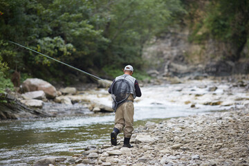 Back view of fisherman walking along mountain river with rod