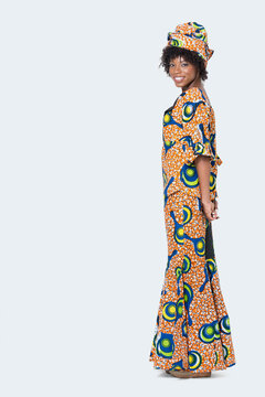 Full length portrait of young woman in African print attire standing over gray background