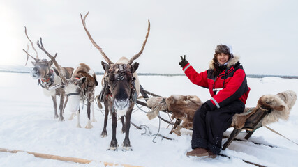 Asian woman in red smile on reindeer sled for toursit or traveler outdoor activity in winter tundra weather. Deer horn cut, pasture animal is symbol for christmas to give present with santa claus. © Chanokporn