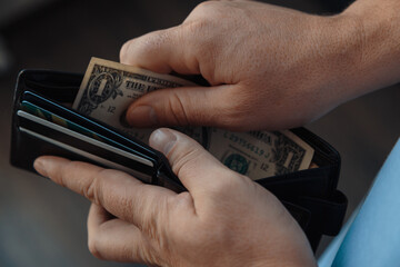 the hands of a working man put one dollar bills in an empty wallet. Poverty concept, crisis.