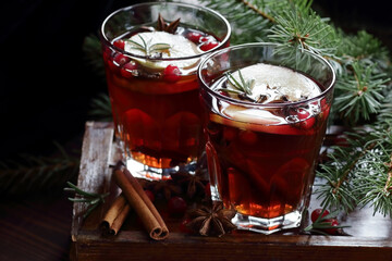 Mulled red wine with cranberry, apple and spices: anise, cinnamon, rosemary and cloves on dark moody black background and fir branches, winter christmas coctail, holiday hot drink, closeup