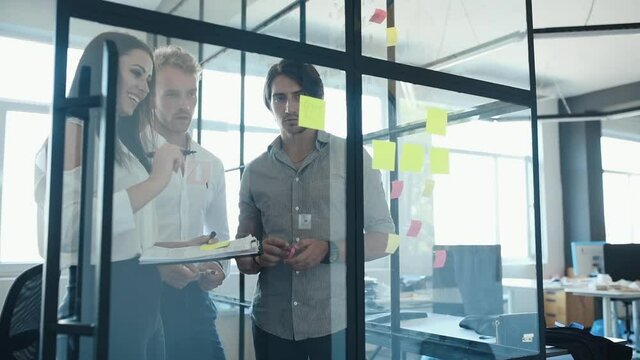 Young business people in formal clothes planning work in the office with paper stickers on the glass.