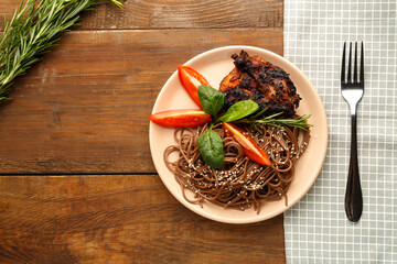 A plate of soba with chicken tomatoes and spinach on a napkin next to a fork on the table.