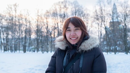 Fototapeta na wymiar Woman traveler asian female in warm black winter outfit with light brown fur smile under sunlight with snow and forest background. Thai lady tourist in cold country nature outdoor hiking activity.