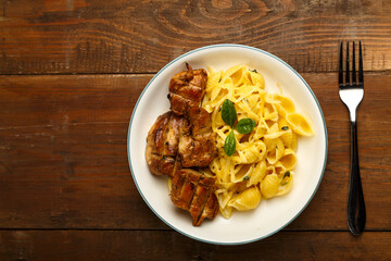 pasta in a creamy sauce with spinach and chicken in a plate on a wooden board next to a fork. copy space