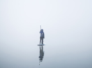 unrecognizable female with paddle on the sup board on the river surrounded of dense fog